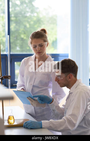 Male student reading record while practicing chemistry experiment in lab Stock Photo
