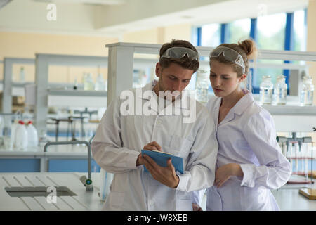 Male student showing clipboard to classmate while practicing chemistry experiment in lab Stock Photo