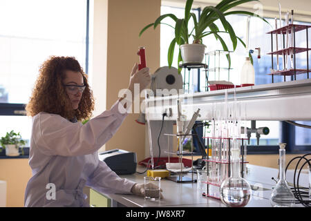 Teenage girl holding pipette while practicing chemistry experiment at desk in lab Stock Photo
