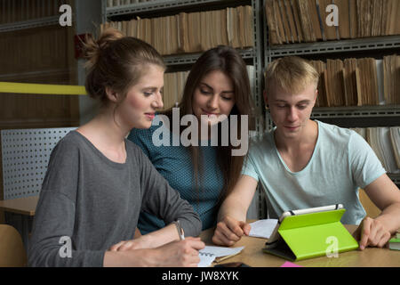 College students looking at tablet computer while studying at desk in library Stock Photo