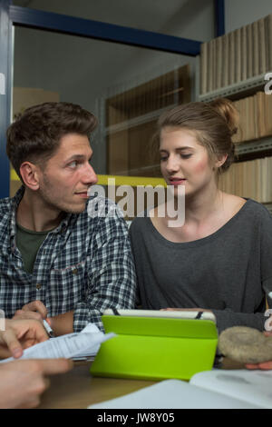College students discussing while studying at desk in classroom Stock Photo