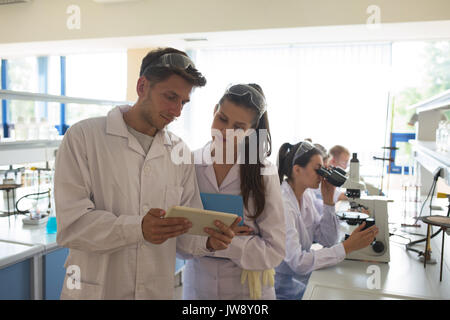 Male student showing tablet computer to friend while standing in lab Stock Photo