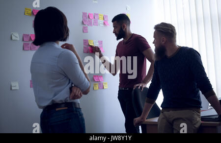 Colleagues discussing over sticky notes in office Stock Photo