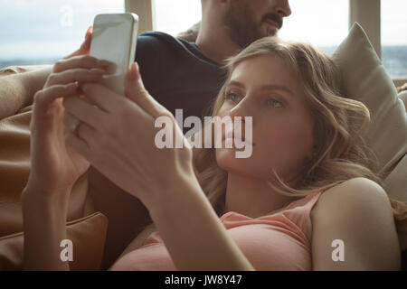 Romantic couple lying on sofa and using mobile phone in living room Stock Photo