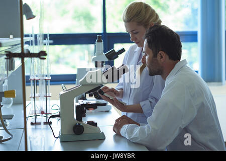University students using digital tablet while doing experiment on microscope in laboratory at college Stock Photo