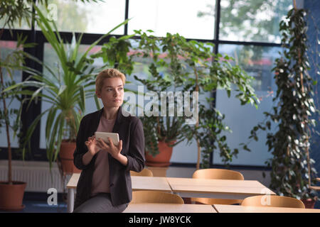 Thoughtful university student using digital tablet in college Stock Photo