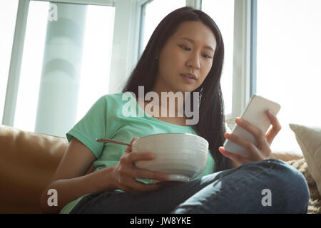 Woman having breakfast while using mobile phone at home Stock Photo