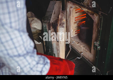 Mid section of craftsman heating metal in furnace in workshop Stock Photo