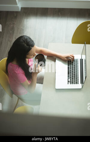 Top view of woman having coffee while using laptop in living room Stock Photo
