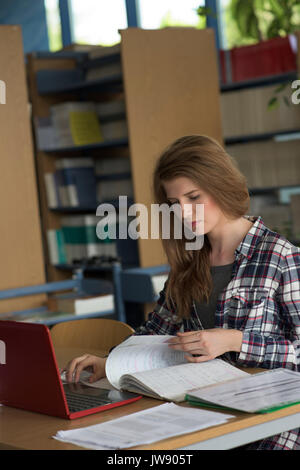 Young female student using laptop while studying at desk in classroom Stock Photo