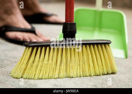 closeup of a young man sweeping the floor with a broom of green synthetic bristles and a green dustpan Stock Photo