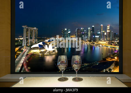 Closeup of a glasses of red wine at windowsill, against night Singapore city view of urban city sky line blurring lights. Singapore. Stock Photo
