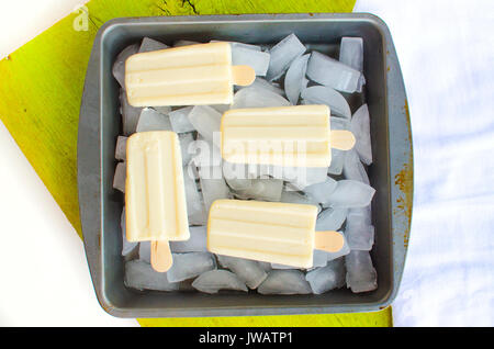 Vanilla ice cream Popsicles melting over tray of ice on summer day.  View looking down from above. Stock Photo