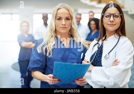 Two young female doctors looking at camera standing in a hospital with the papers. Stock Photo