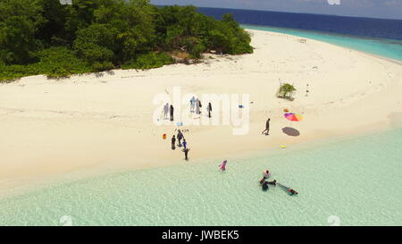 Maldivian uninhabited island with white sandy beach while a family have a picnic in coral islands beach Stock Photo