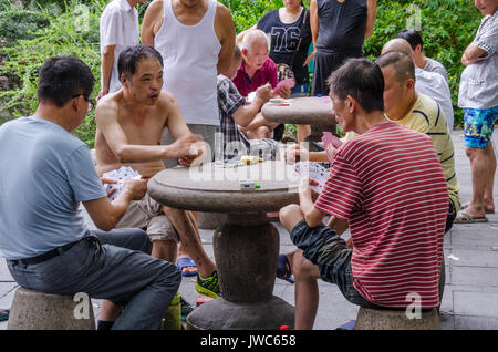 Men sitting outside at tables in The People's Park in Shanghai playing cards, Stock Photo