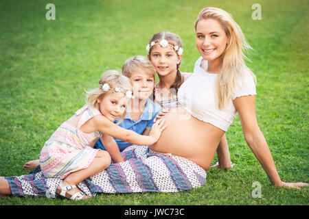 Mother of many children, cute blond pregnant woman with her three older children with pleasure spending time outdoors, happy family life Stock Photo