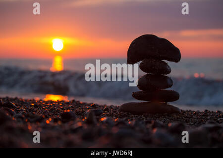 Silhouette of a rock cairn stacked on the beach of Lake Superior at sunset. Stock Photo