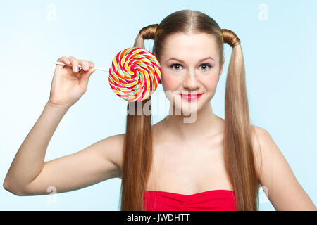 Beautiful playful young freckled girl with lollipop on blue background