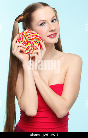 Beautiful playful young freckled girl with lollipop on blue background