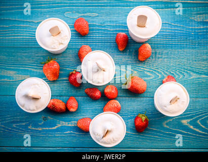 Ice cream in cups with strawberries on a blue wooden background