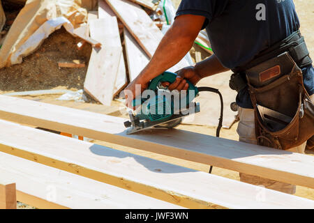 Worker hands details of wood cutter machine with a circular saw and wooden  board. Circular cutting saw in action. Stock Photo