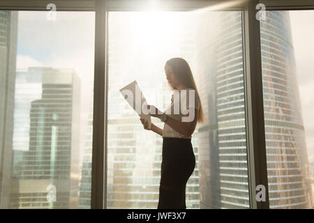 Busy serious businesswoman holding reading document, standing ne Stock Photo