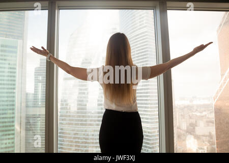 Confident businesswoman spreading hands standing at big window,  Stock Photo