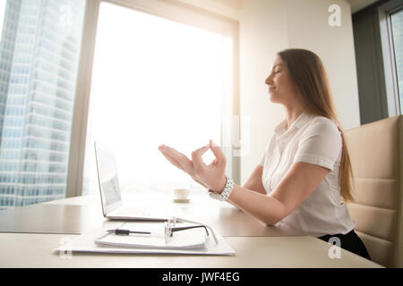 Calm peaceful businesswoman practicing yoga at work, meditating  Stock Photo