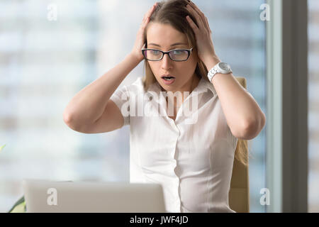 Surprised shocked businesswoman looking at laptop, head in hands Stock Photo