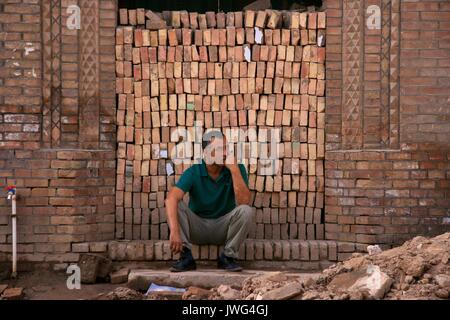 Man seated in front of a pile of bricks in old town Kashgar Stock Photo