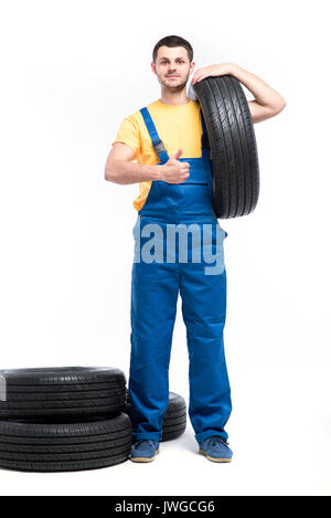 Serviceman in blue uniform holds tire in hand, white background, repairman with tyres Stock Photo