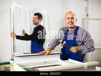 Two smiling professional workers in blue coverall with different PVC windows and doors Stock Photo