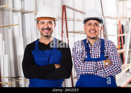 Two positive specialists in helmets and workwear posing at workshop Stock Photo