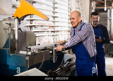 Couple of positive workmen in overalls near cutter - lathe machine at factory Stock Photo