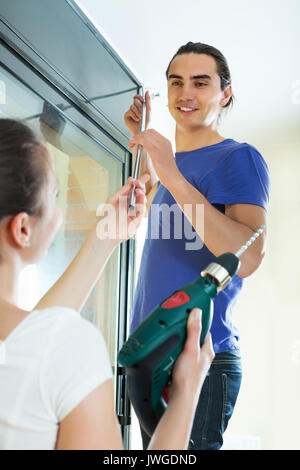 Smiling young man and woman hanging curtains at window Stock Photo