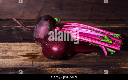 Two whole fresh beets with a tops on a brown wooden table Stock Photo