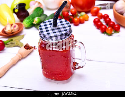 Freshly made juice from a ripe red tomato in a glass jar with a straw on a white wooden background Stock Photo