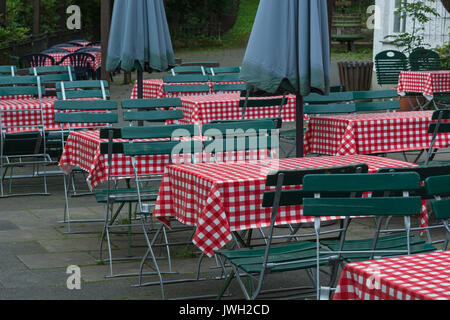 Empty beer tables with red white tablecloth and green wooden chairs in a public beer garden. Stock Photo