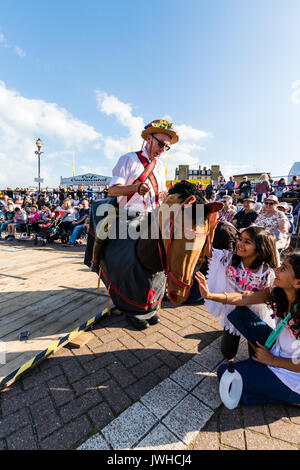 Broadstairs yearly folk week festival. Man riding hobby horse, the Harwich Morris beast, fool, in front of audience and children. One young girl child reaching out to touch the horse's head. Stock Photo