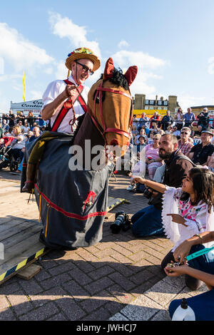 Broadstairs yearly folk week festival. Man riding hobby horse, the Harwich Morris beast, fool, in front of audience and children. One young girl child reaching out to touch the horse's head. Stock Photo