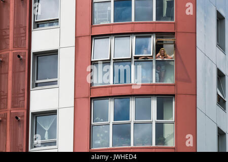London, UK. 12th August 2017. Women greet the Focus E15 Mothers march from a high window in Tanner Point in Plaistow, another Newham Council tower block with the same unsafe cladding as Grenfell Tower,. THe march demanded safe homes, not social cleansing in East London.  They then continued to the Carpenters Estate in Stratford largely emptied of people over 10 years ago and intends to demolish, for a ‘hands around the Carpenters Estate’ solidarity event against decanting, demolition and social cleansing. Peter Mars Credit: Peter Marshall/Alamy Live News Stock Photo