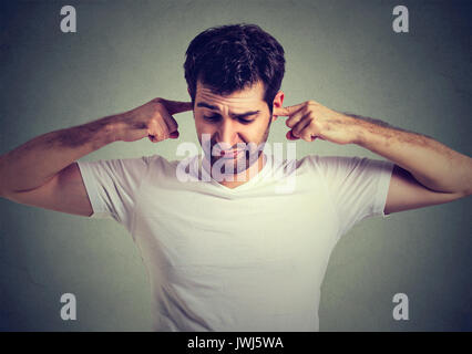 angry unhappy annoyed man plugging his ears with fingers over gray dark background Stock Photo