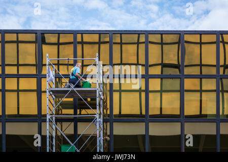 Windows cleaning work, man worker  washing glasses windows at height in lifting platform. Window washing on office building in crane bucket. Stock Photo