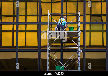 Windows cleaning work, man worker  washing glasses windows at height in lifting platform. Window washing on office building in crane bucket. Stock Photo