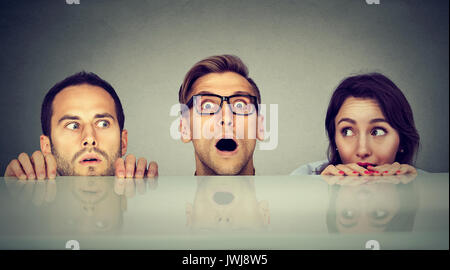 Scared young people two men and a woman hiding peeking form under the table Stock Photo