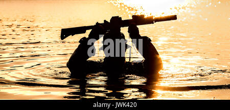 Silhouette of special forces with rifle in action during raid crossing river in the jungle waist deep in the water, with weapons over his head Stock Photo