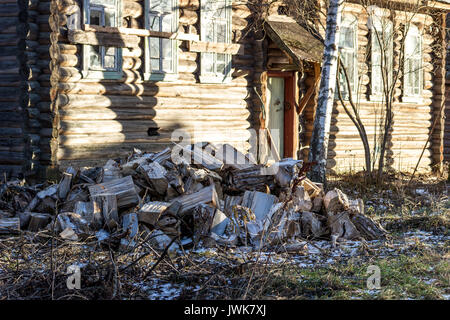 Sawn trunks of trees for splitting firewood. In the background is an old wooden house. Stock Photo