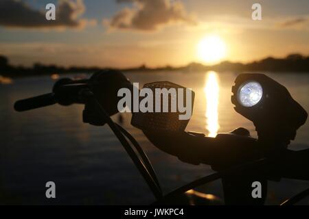 Bicycle Light Illuminated on Handlebars Against Sunset on Lake Stock Photo