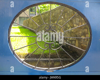 A secluded garden through a wrought iron window in a blue gateway Stock Photo